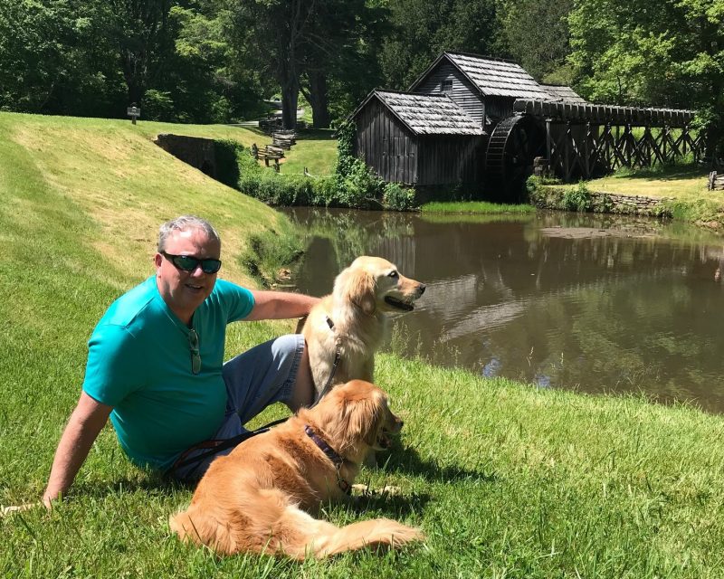 Robert "Bobby" Grisso sitting on a grassy lawn with two golden retrievers