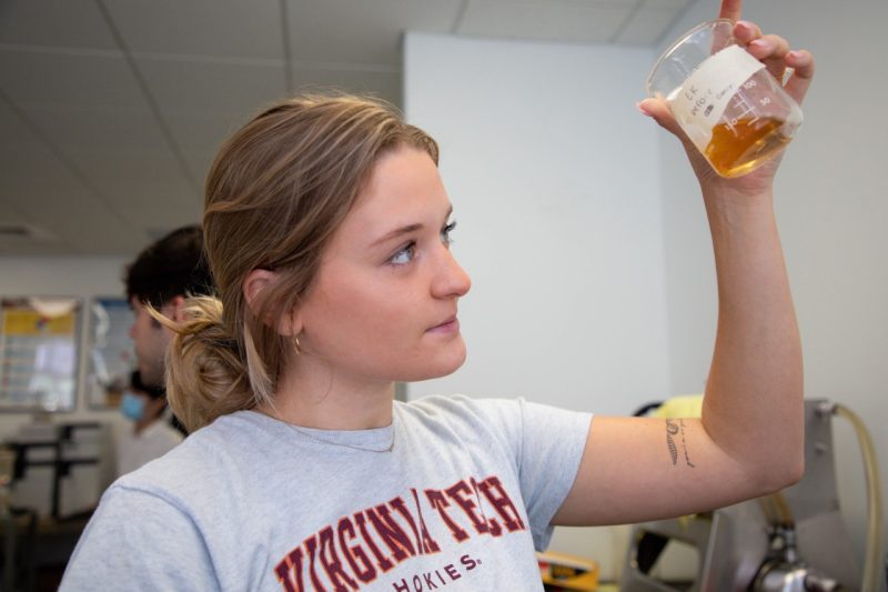 Virginia Tech Biological Systems Engineering student holds a beaker with discolored liquid above their line of sight to observe a reaction.