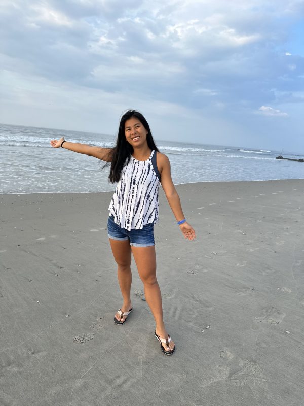 A young lady standing on the beach smiling at the camera