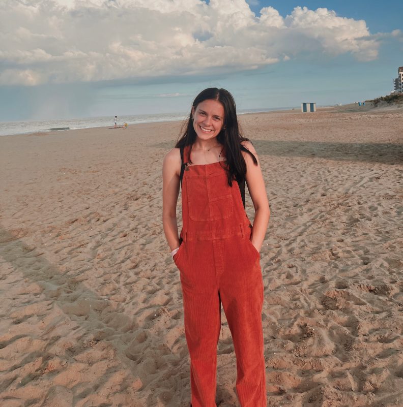 a young woman stands on the beach smiling at the camera